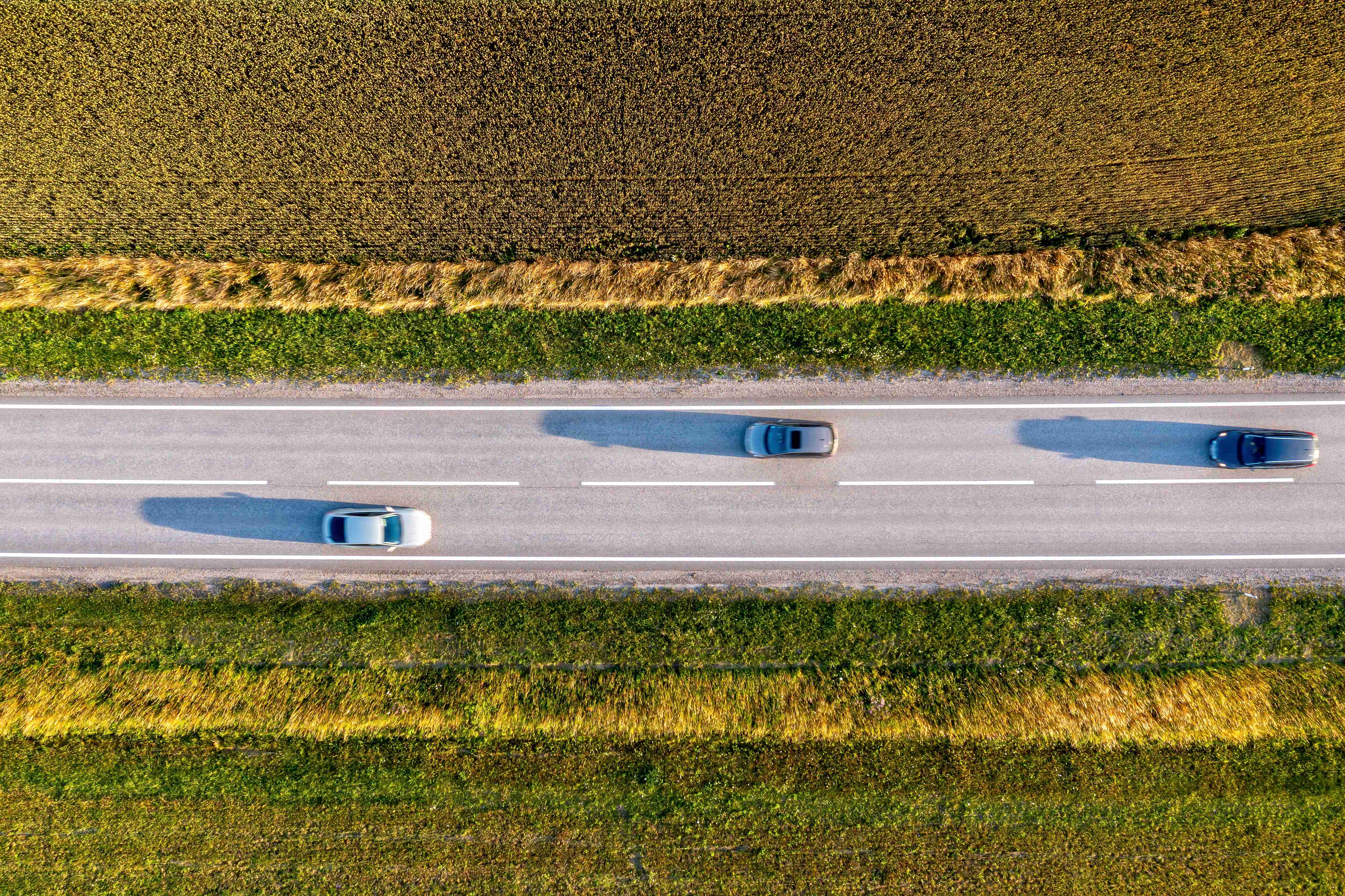 Luftaufnahme von Autos, die auf einer von Feldern umgebenen Landstraße fahren