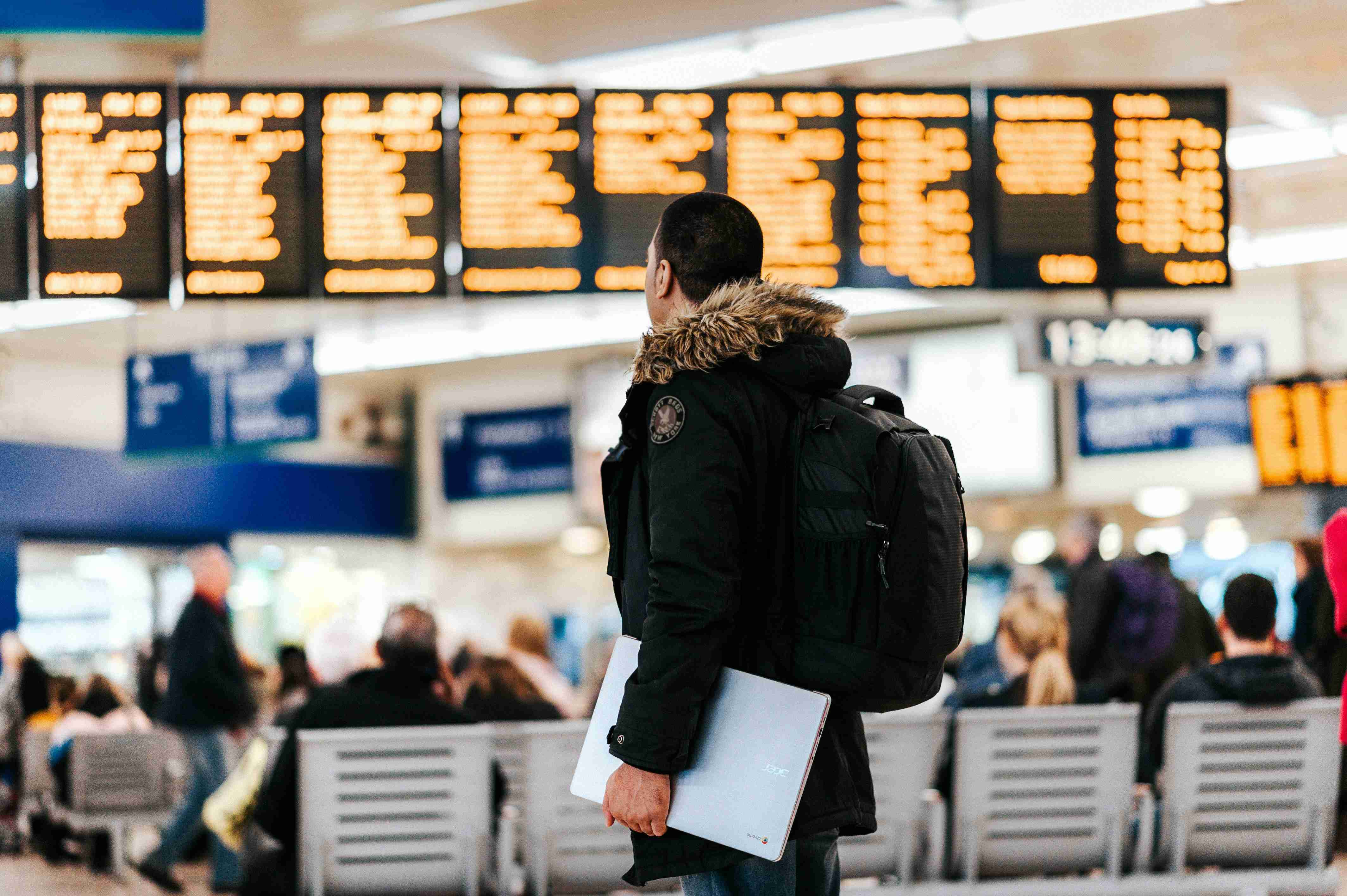 man-standing-inside-airport-looking-at-led-flight-schedule