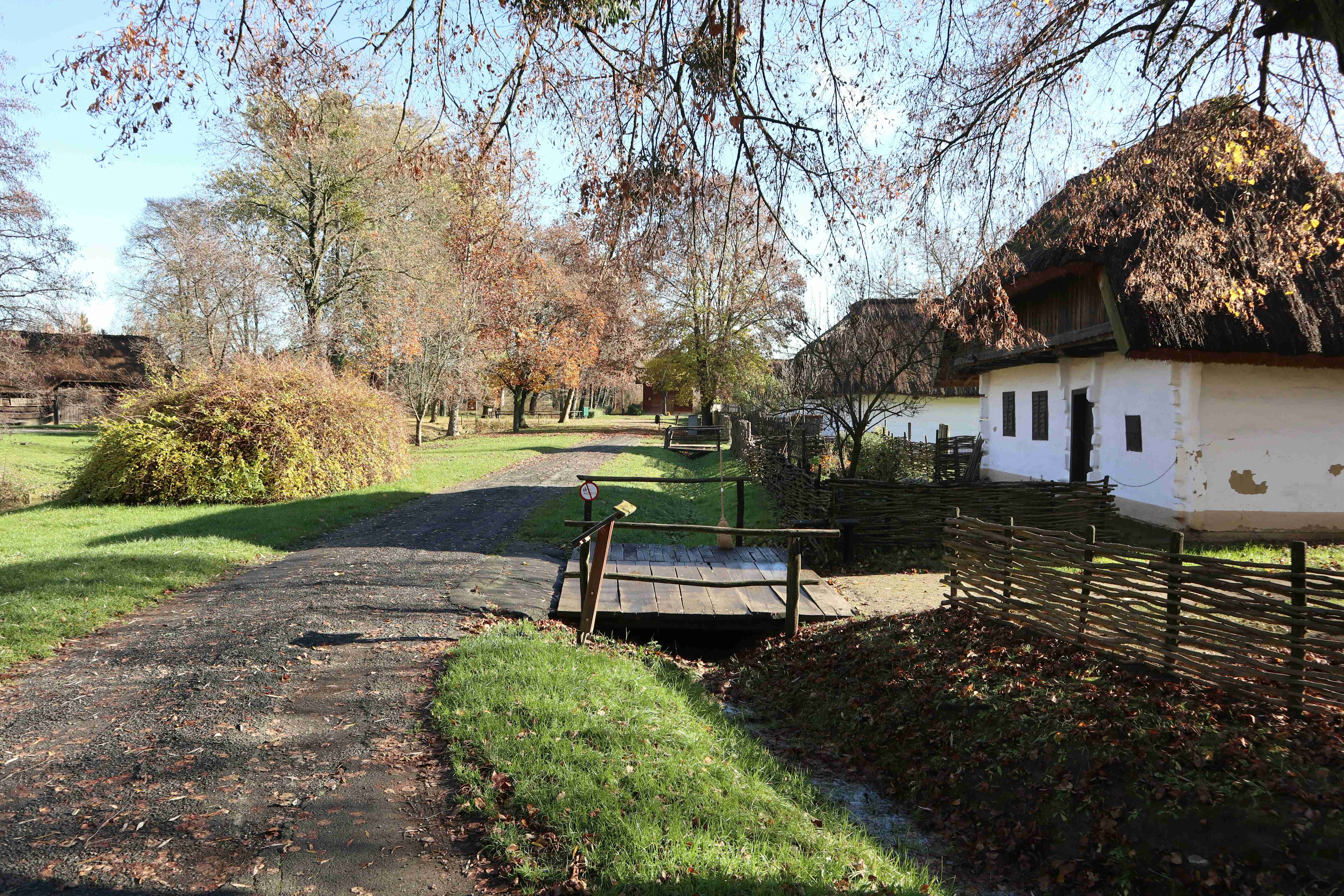 a-white-house-with-a-thatched-roof-next-to-a-dirt-road