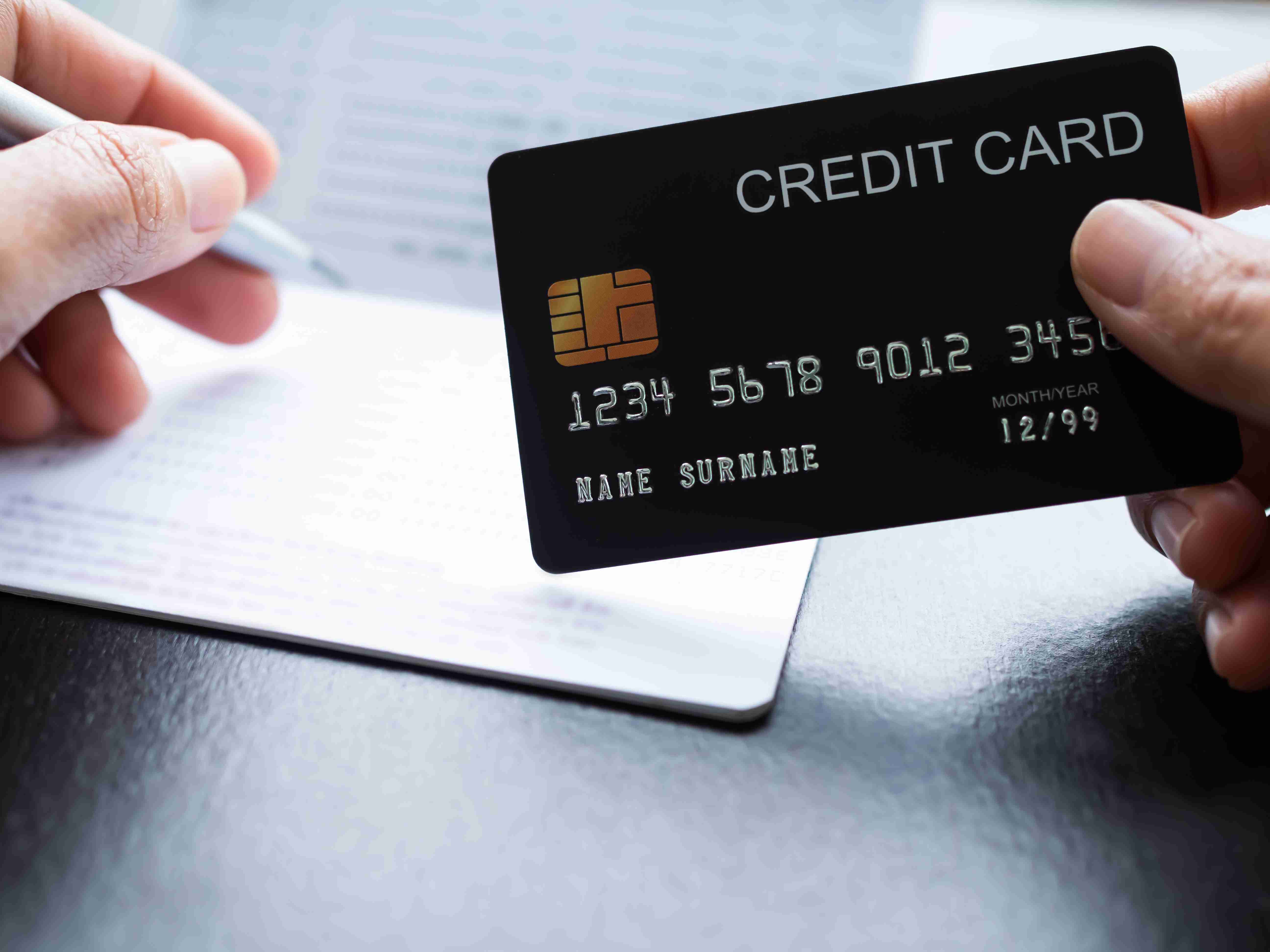 Prst držící kreditní kartu s rozmazaným bankovním účtem a perem