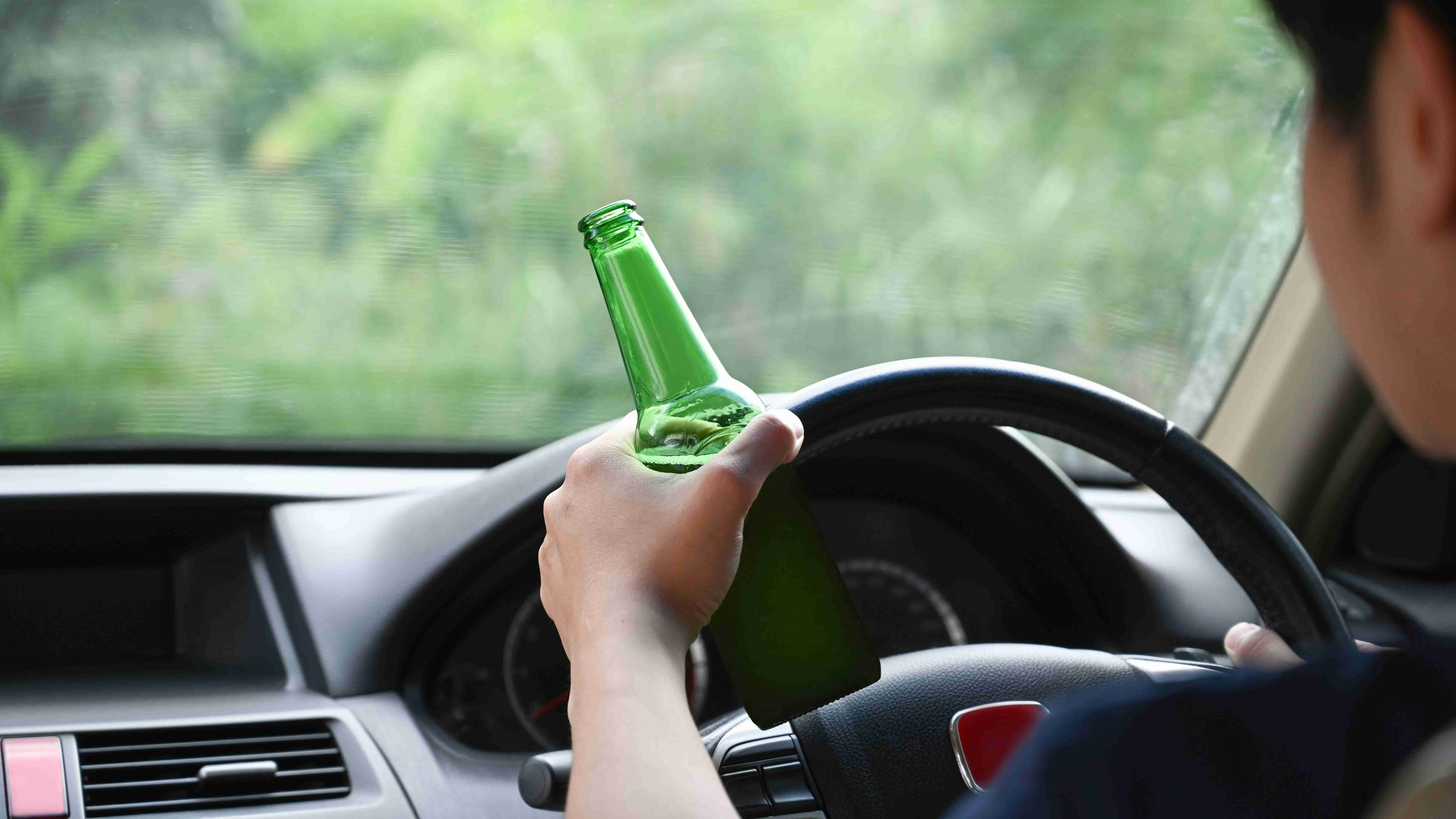 man driving a car while holding a bottle of beer