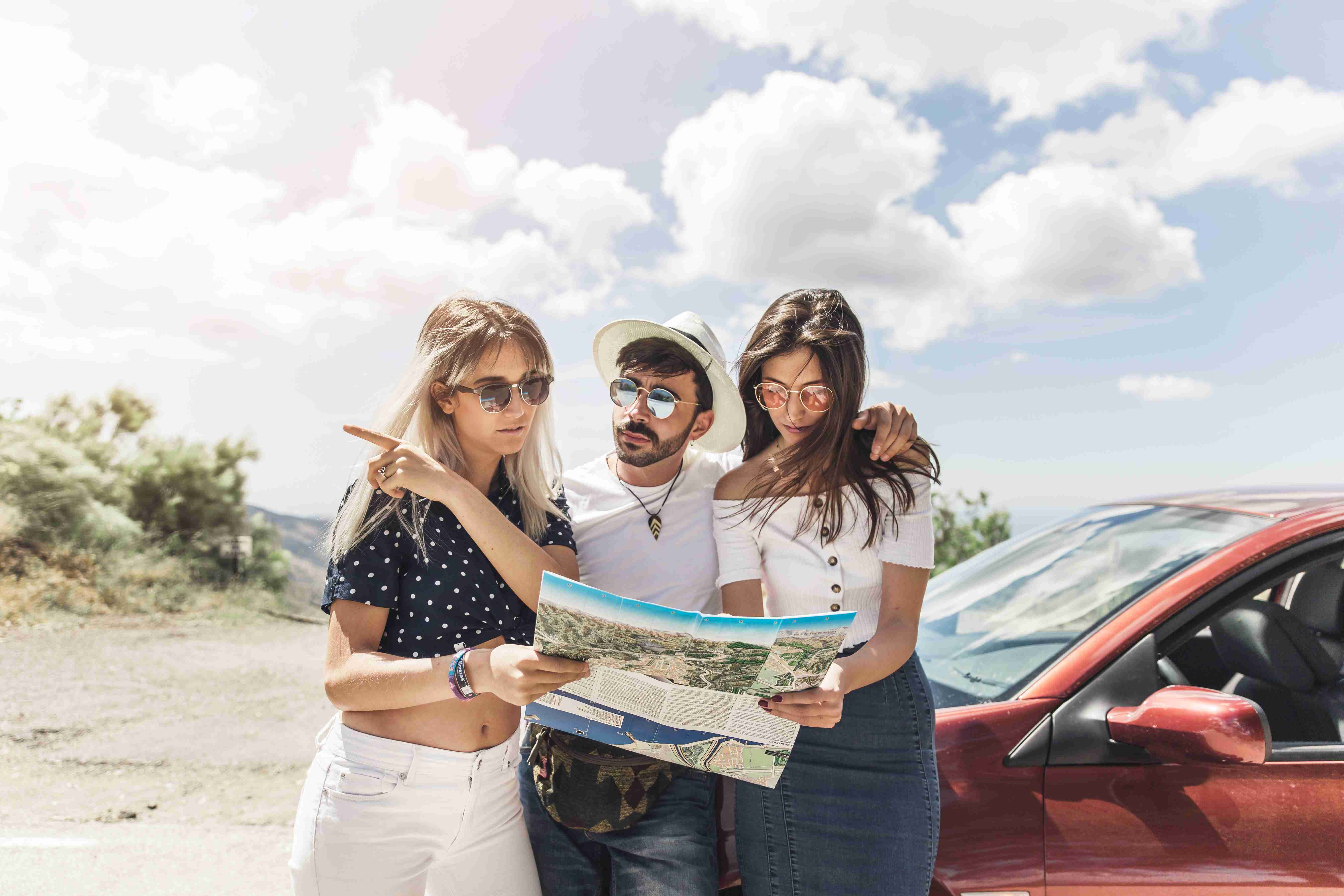 group friends standing near car looking map