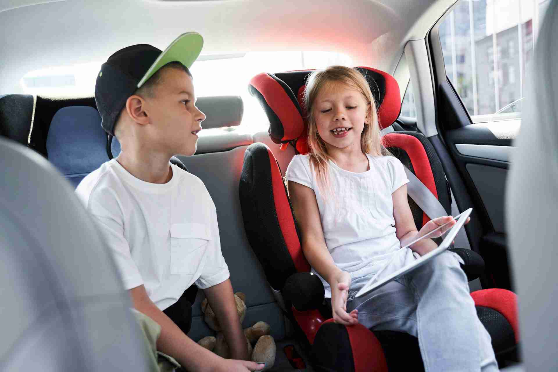 Jolly cute boy and girl are sitting in safe car seats and using digital tablet photo
