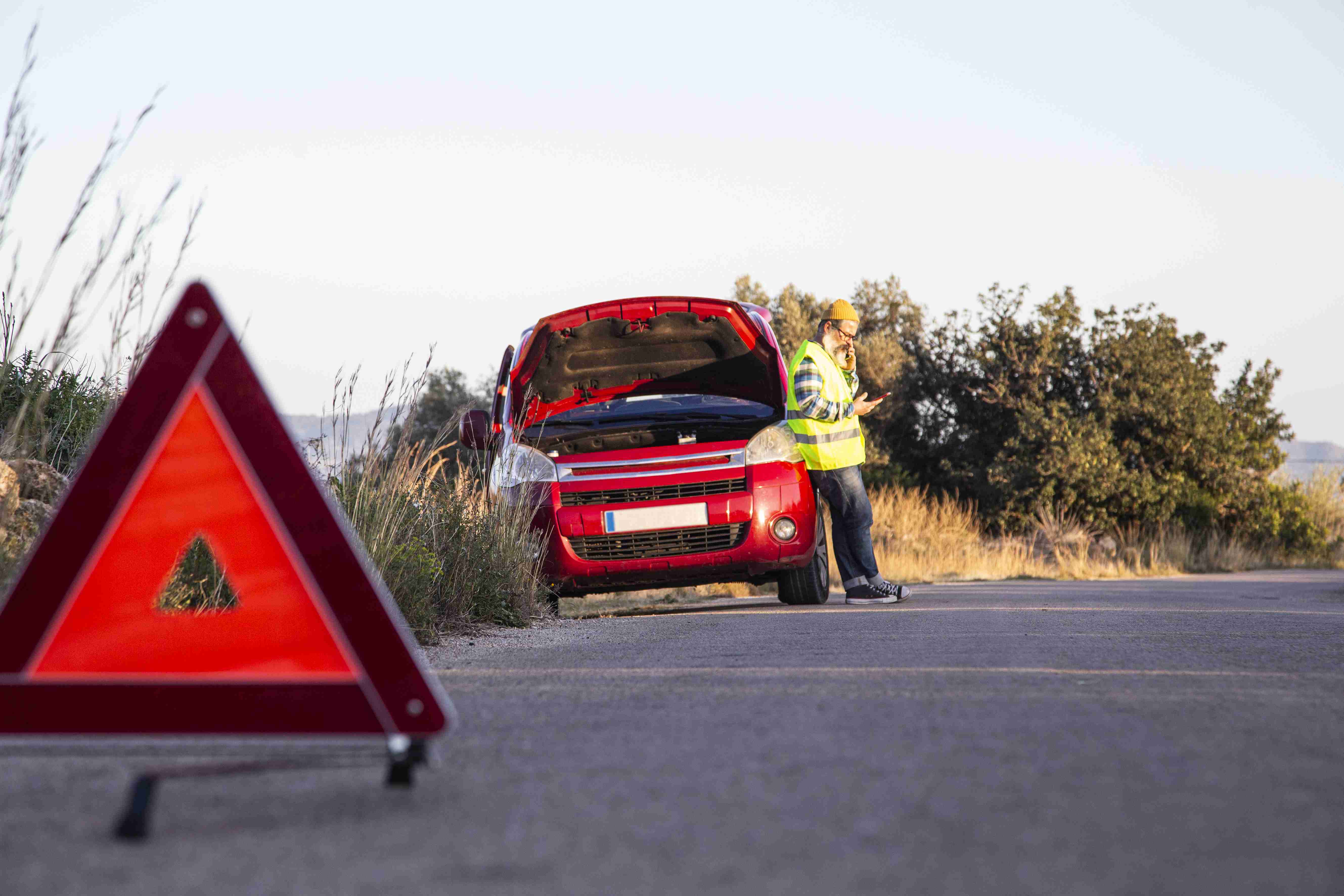 Man with relaxed attitude stranded on the road next to the broken down car