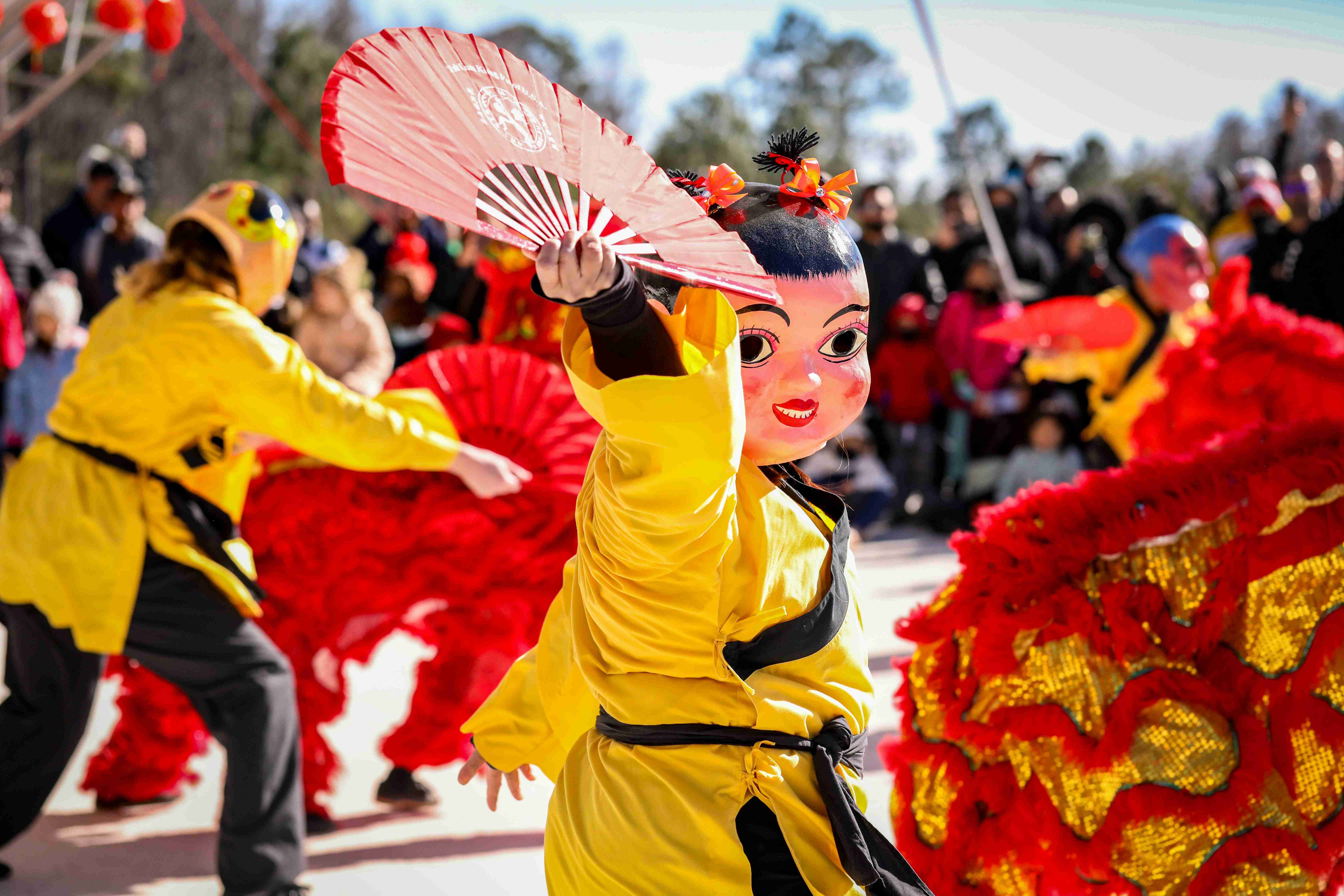a woman in a yellow dress holding a pink fan