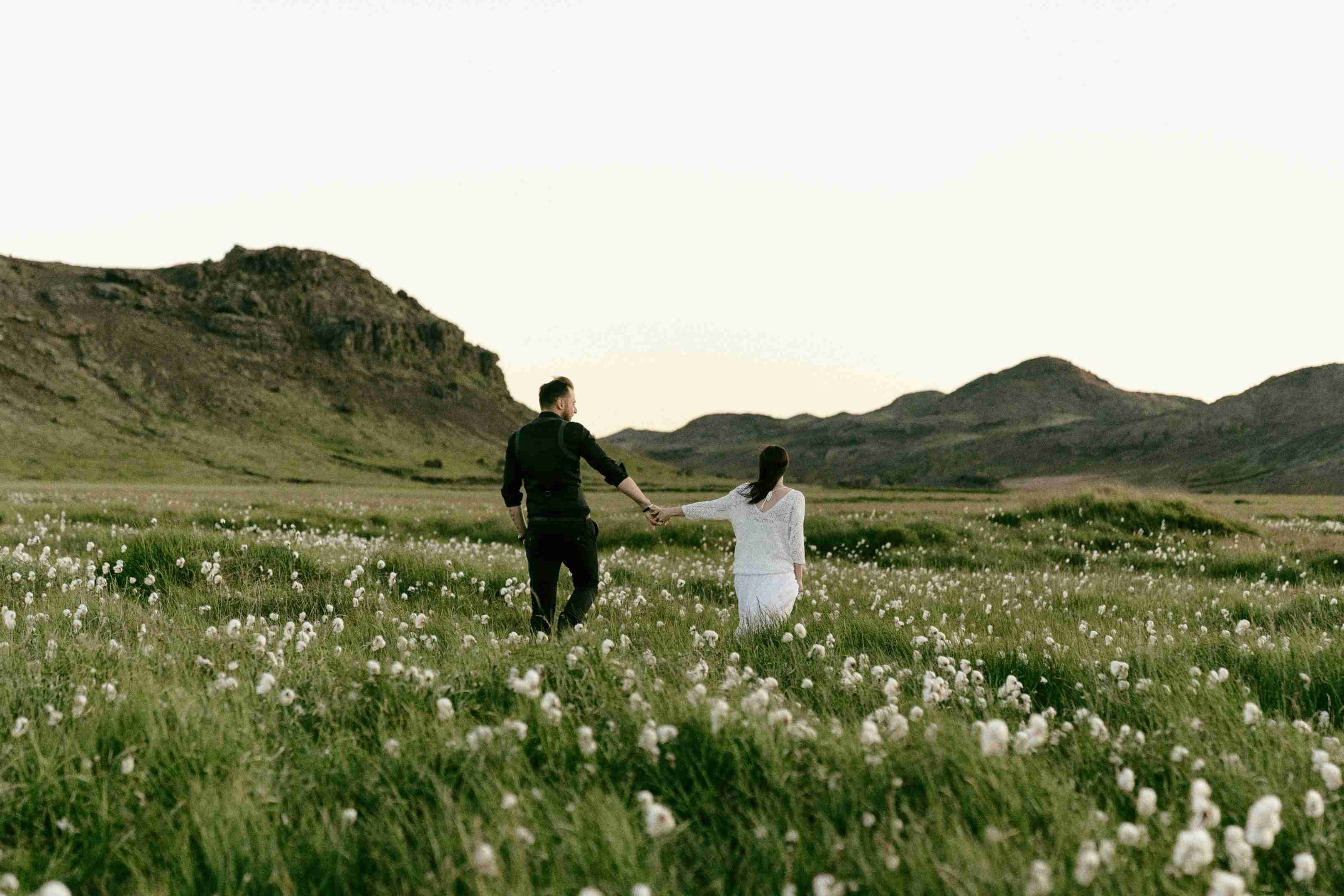 a-couple-walking-hand-in-hand-on-grass-field