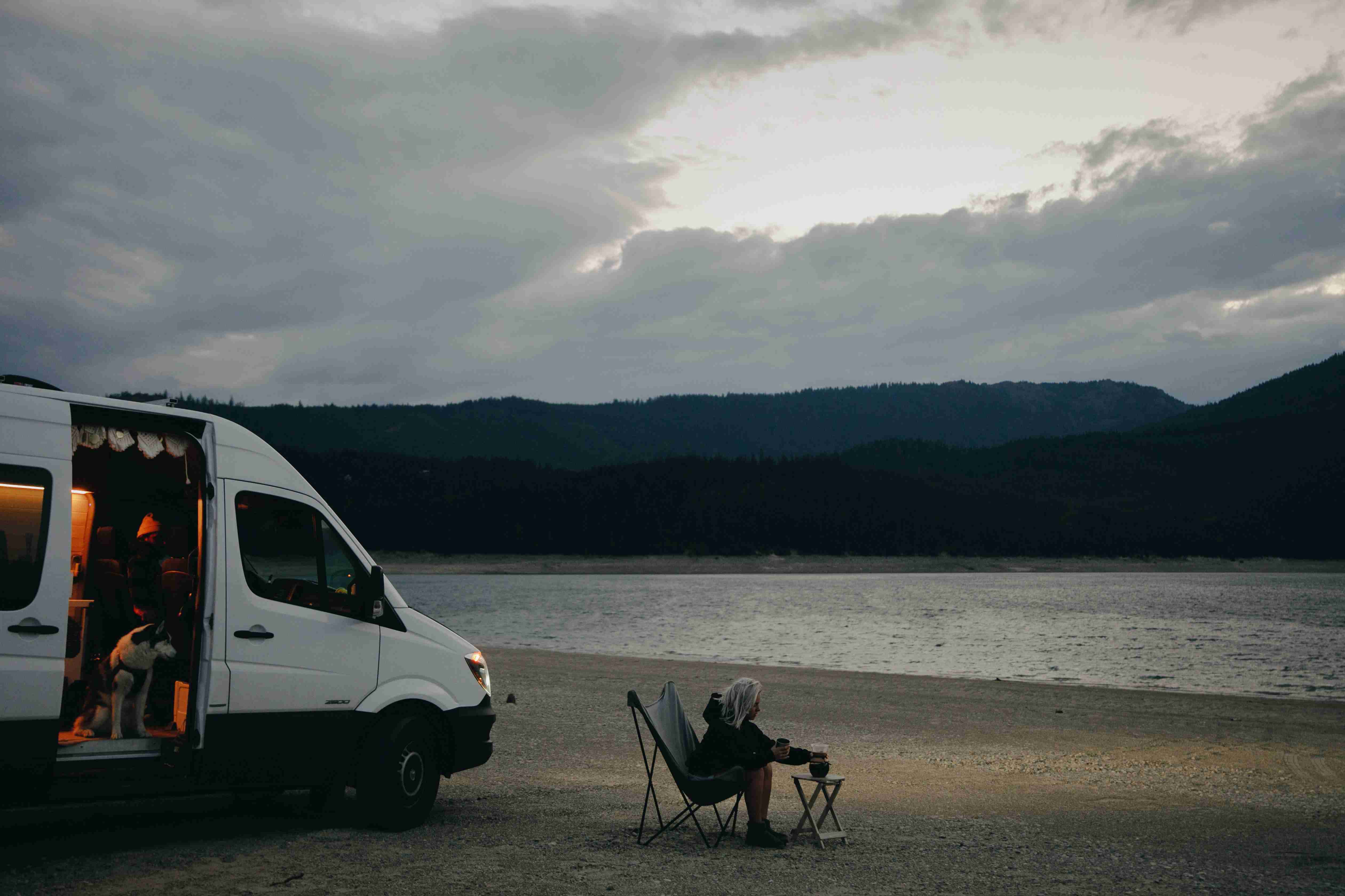 woman-sitting-on-a-folding-chair-on-a-beach-near-a-campervan