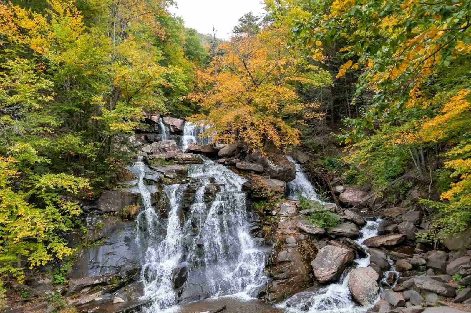 Vattenfall i flera nivåer som rinner över klippor omgivet av pulserande höstlövverk
