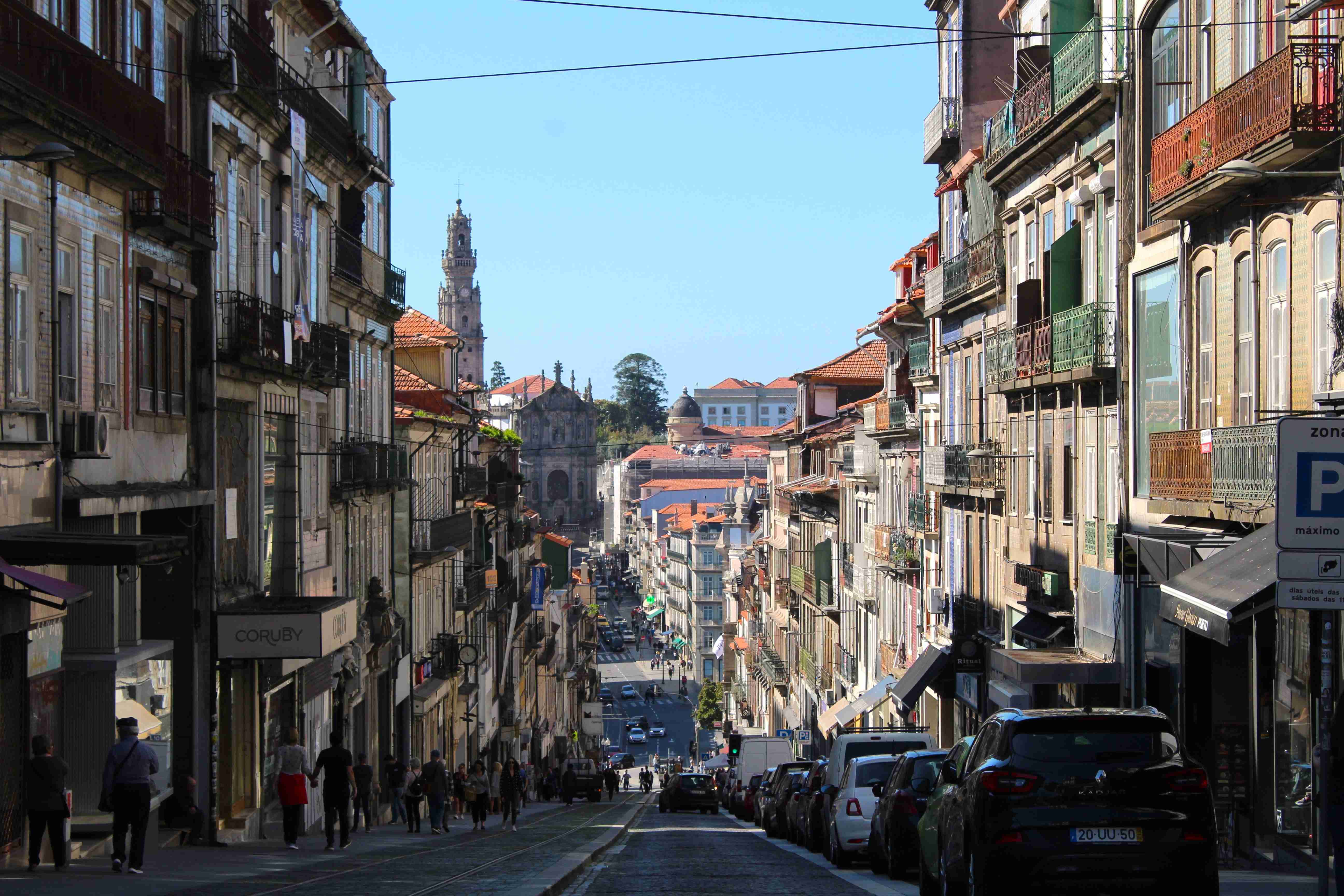 Vue de la Rua dos Clérigos, avec piétons et voitures garées, Tour des Clérigos sous un ciel bleu clair.