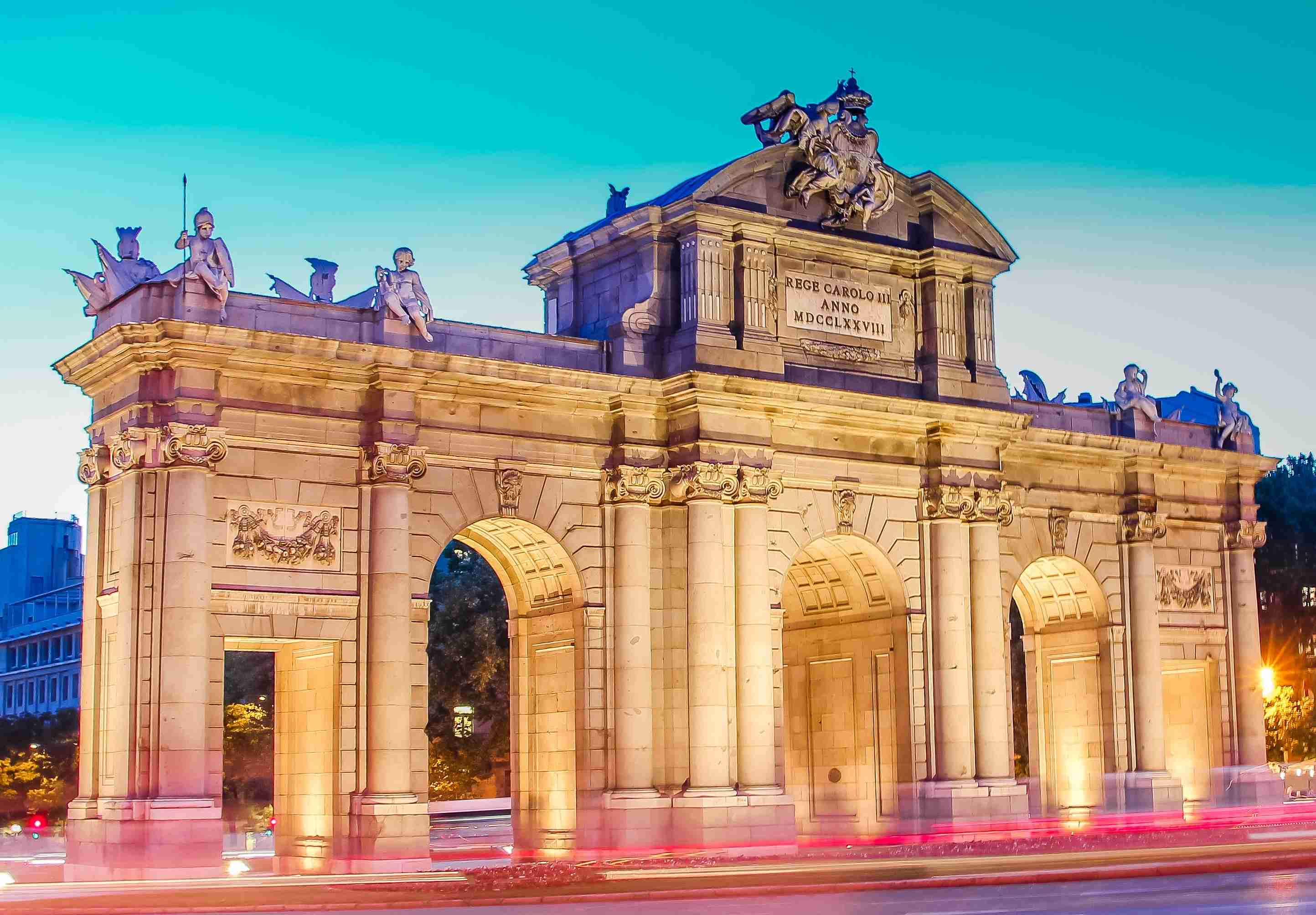 Soumraková obloha za osvětleným historickým obloukovým monumentem.