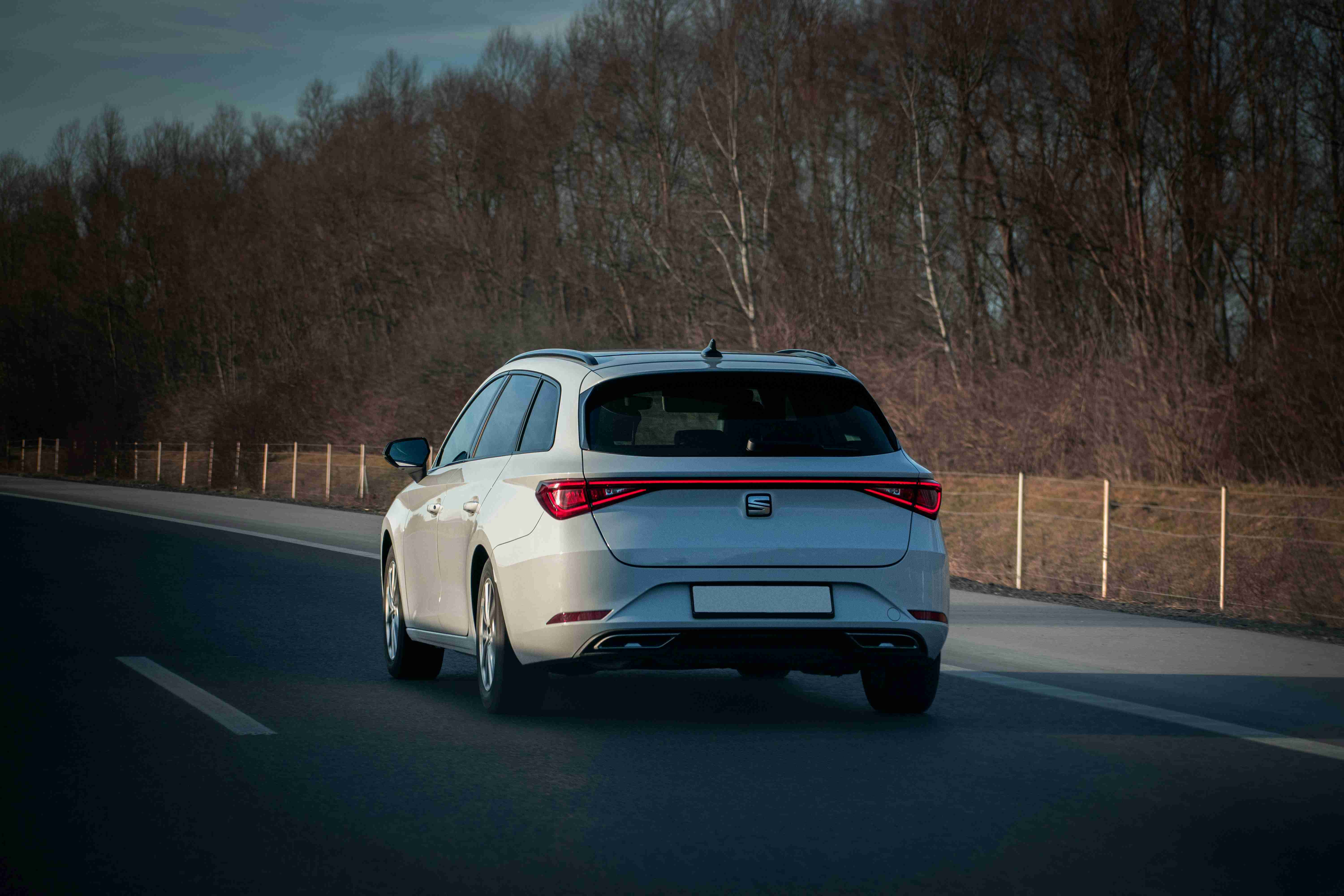 a white car driving down a road next to a forest
