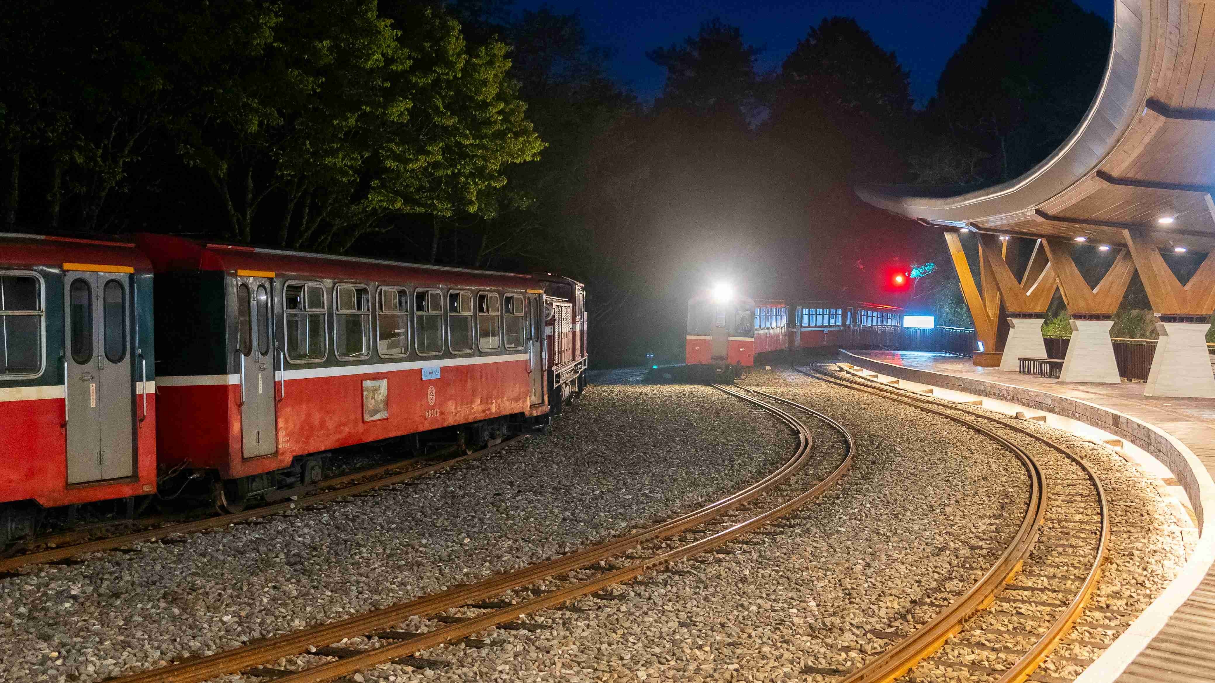 a red train traveling past a train station at night